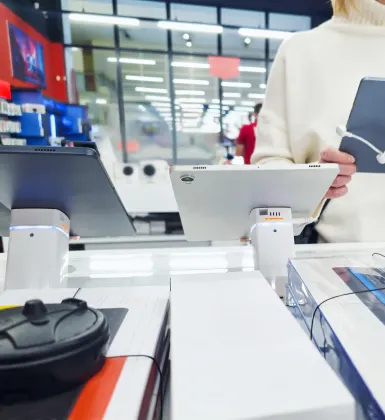 electronics on display in the foreground seen from behind with a woman demoing some in the background