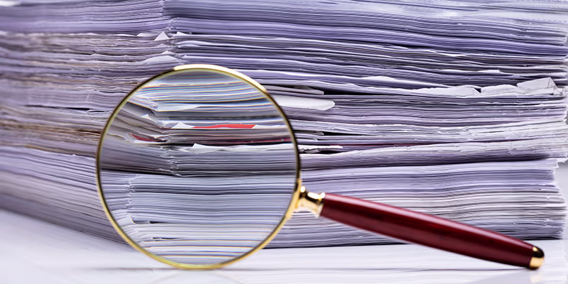 Close-up Of Magnifying Glass On Background Of The Stacked Paper Files