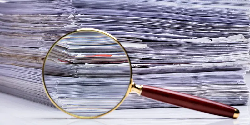 Close-up Of Magnifying Glass On Background Of The Stacked Paper Files